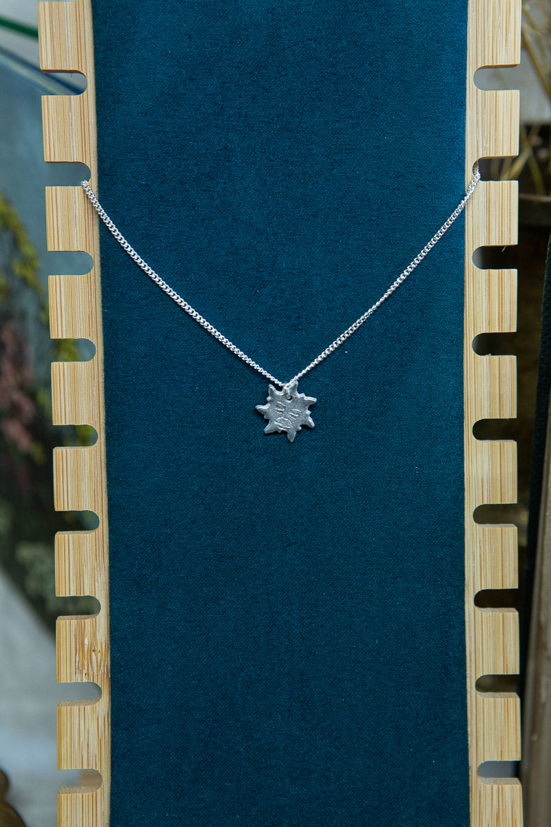 A handmade fine silver sun necklace, each hand carved with different facial expressions.