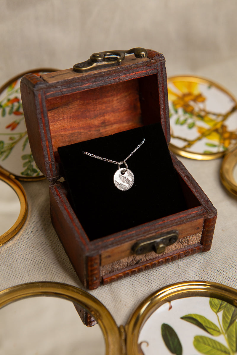 Fern leaf imprinted sterling silver round pendant on a figaro chain.