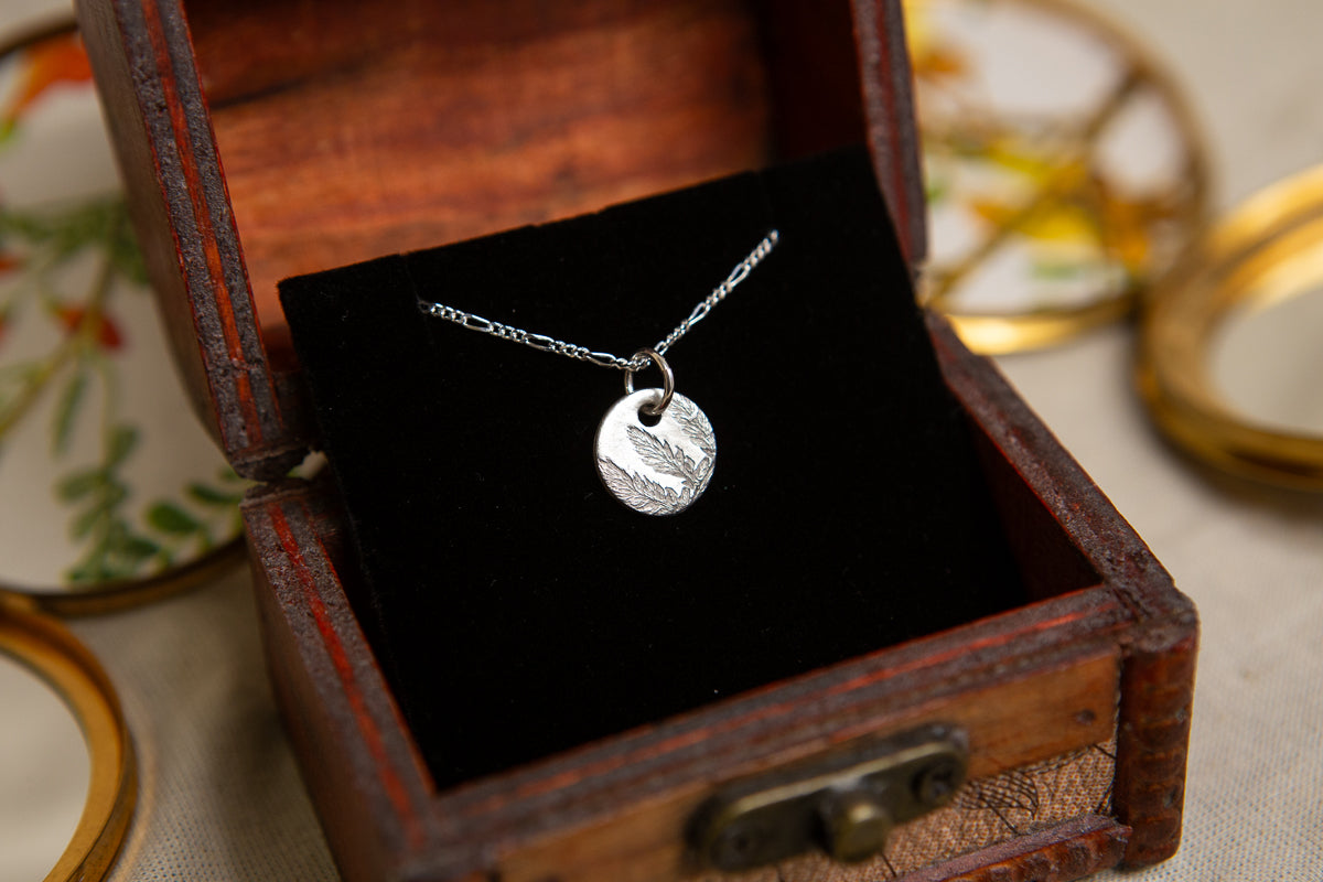 Fern leaf imprinted sterling silver round pendant on a figaro chain.