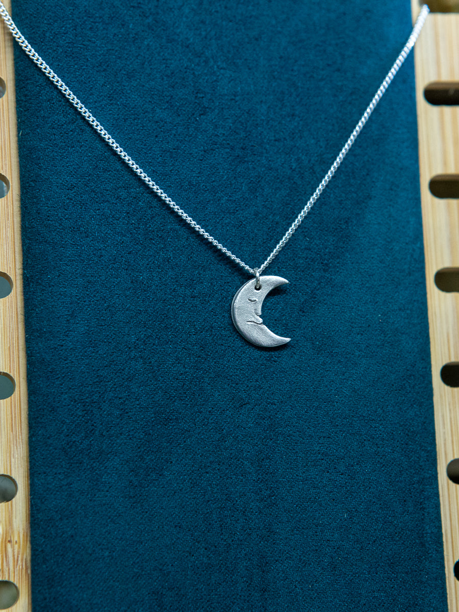 A handmade fine silver moon necklace, each hand carved with different facial expressions.