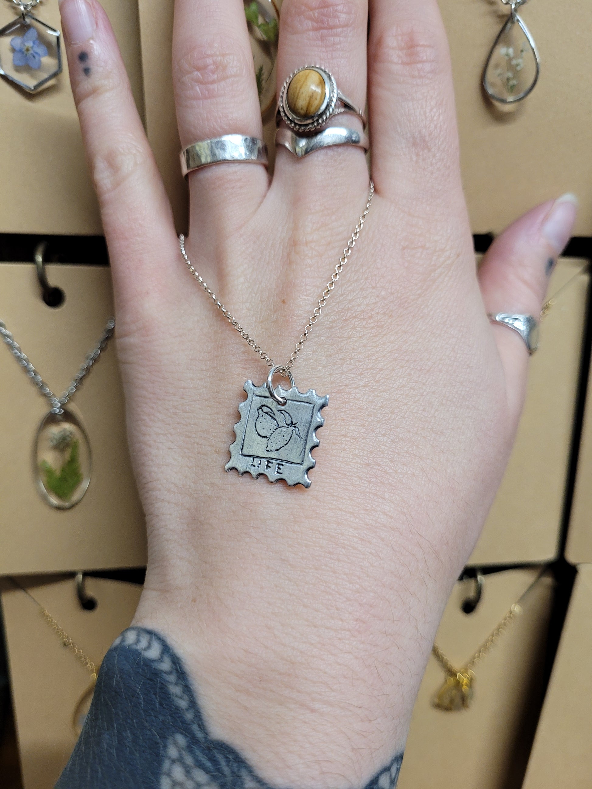 Stamp design fine silver pendant depicting some hand carved lemons with the inscription 'LIFE' below 