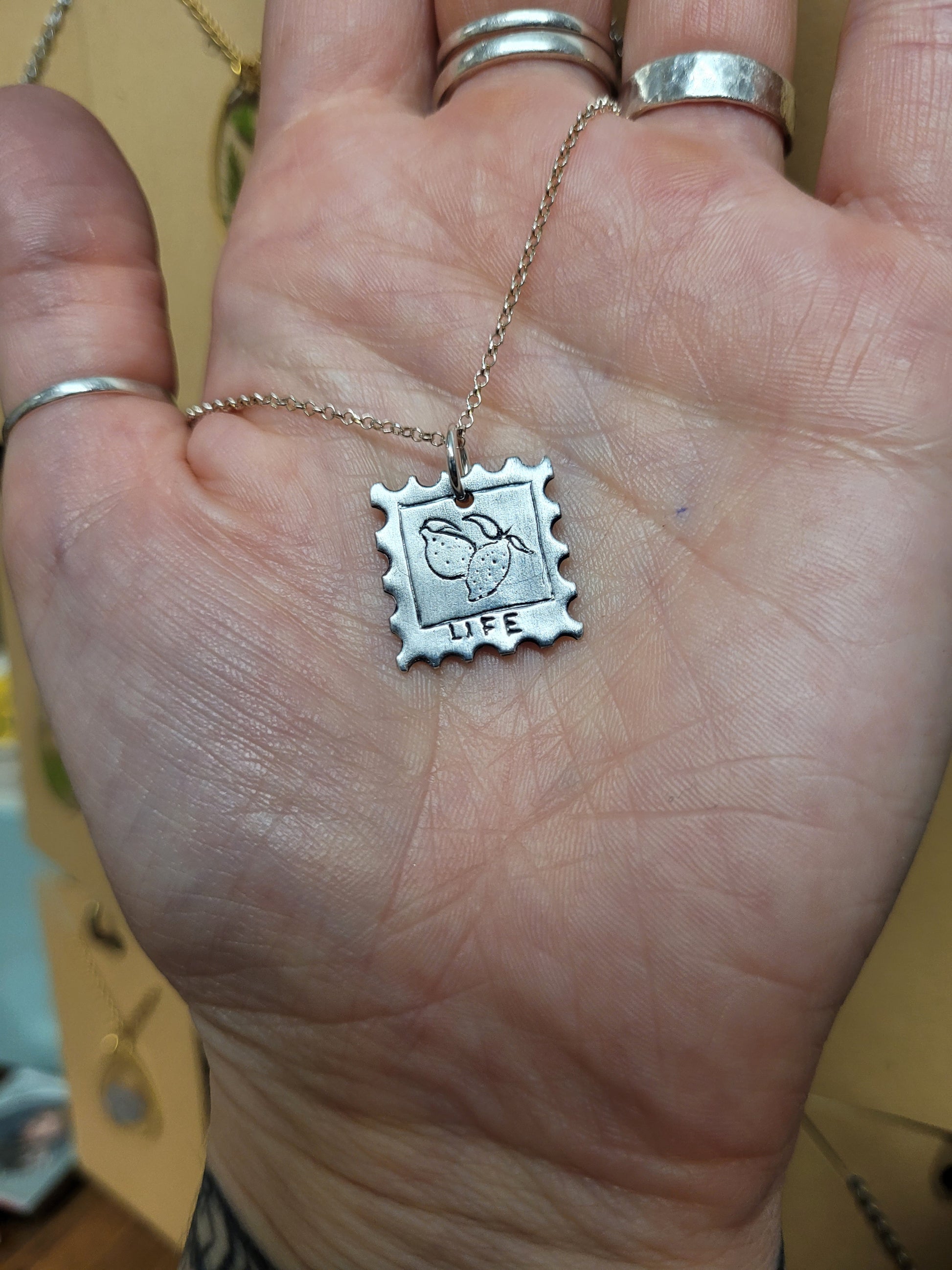 Stamp design fine silver pendant depicting some hand carved lemons with the inscription 'LIFE' below 