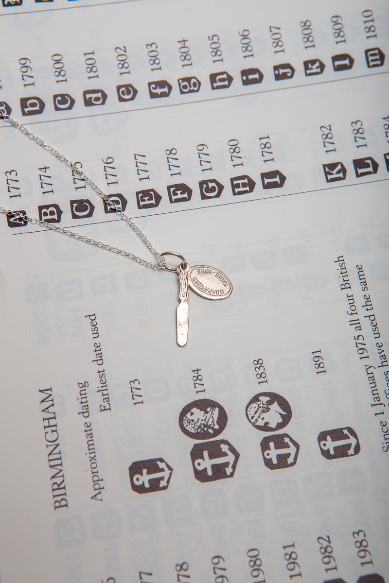 A tiny sterling silver butter knife and guaranteed tableware tag on a necklace.