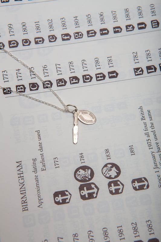 A tiny sterling silver butter knife and guaranteed tableware tag on a necklace.