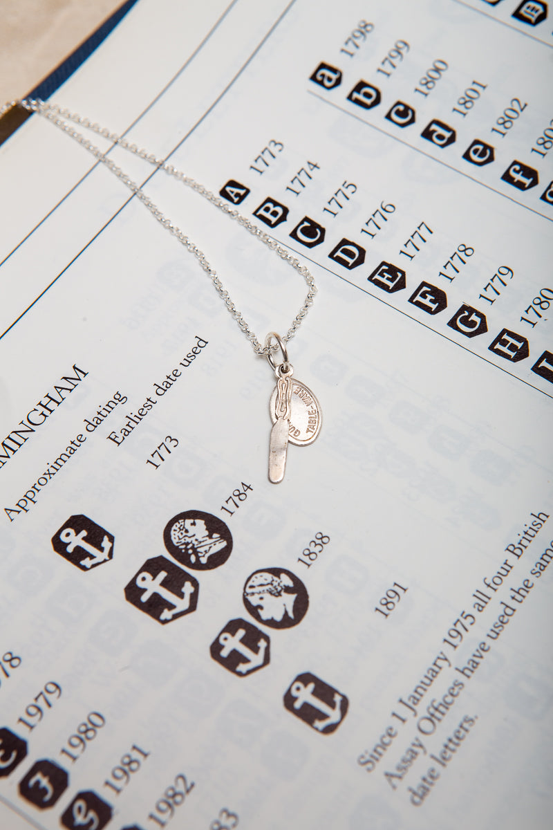 A tiny sterling silver butter knife and guaranteed tableware tag on a necklace.