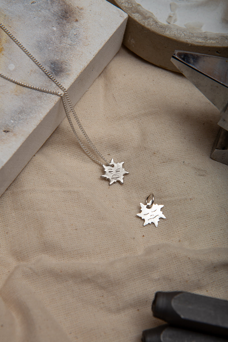 A handmade fine silver sun necklace, each hand carved with different facial expressions.