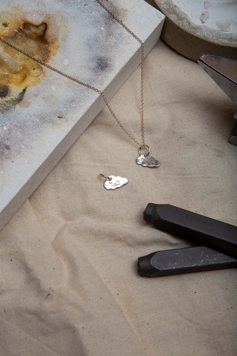 A handmade fine silver cloud necklace, each hand carved with different facial expressions.