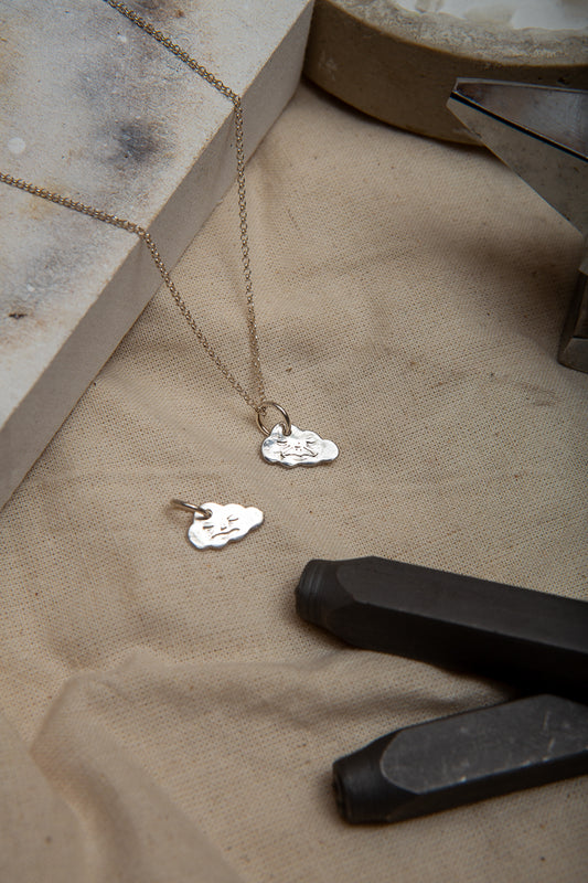 A handmade fine silver cloud necklace, each hand carved with different facial expressions.