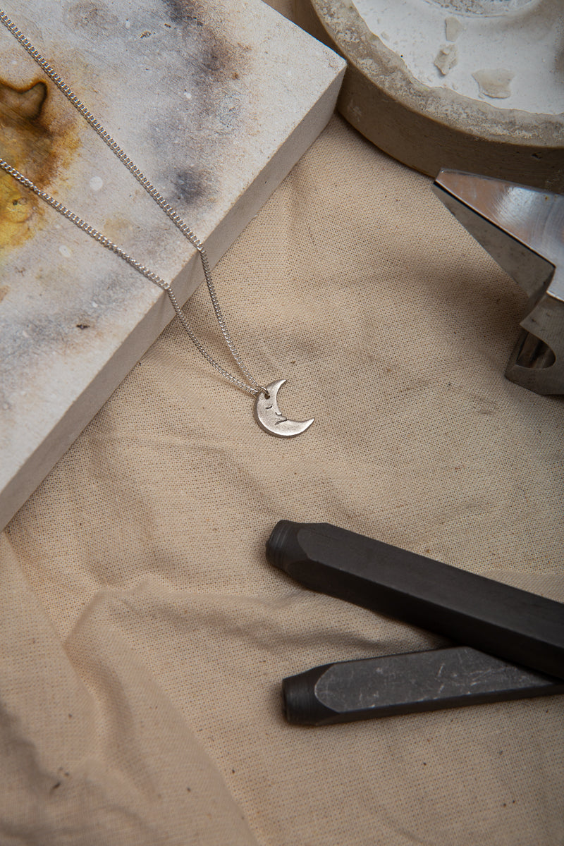 A handmade fine silver moon necklace, each hand carved with different facial expressions.