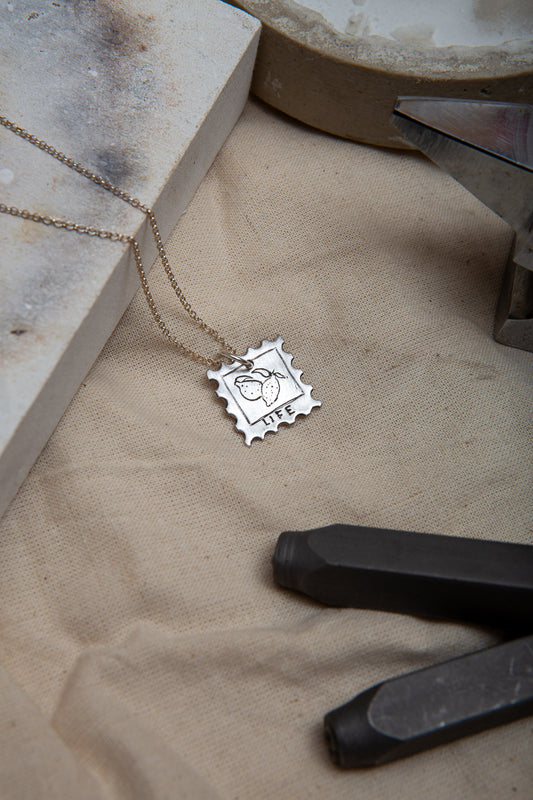 Stamp design fine silver pendant depicting some hand carved lemons with the inscription 'LIFE' below 